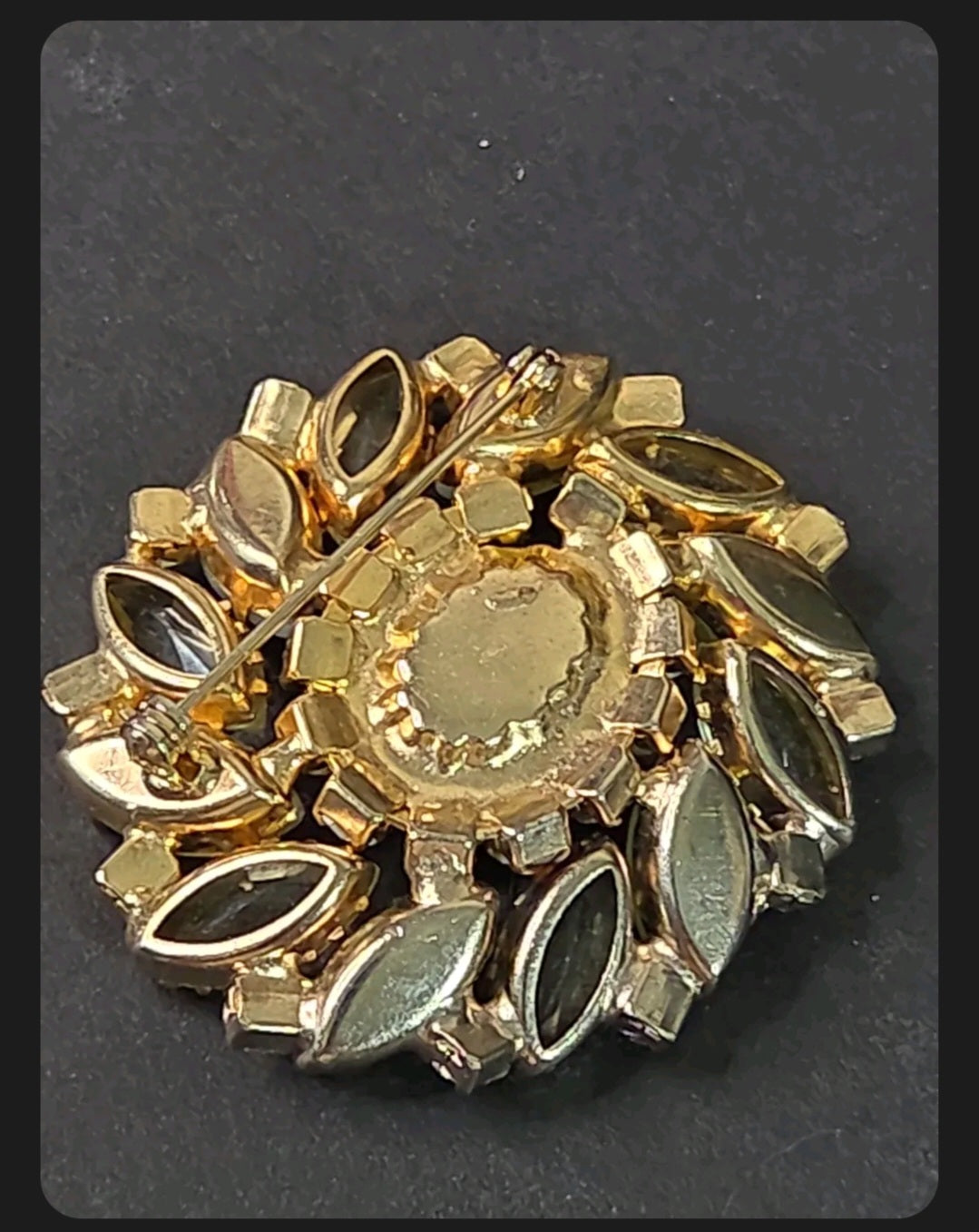 Back of a vintage gold-tone brooch showing the pin, hinge and safety clasp