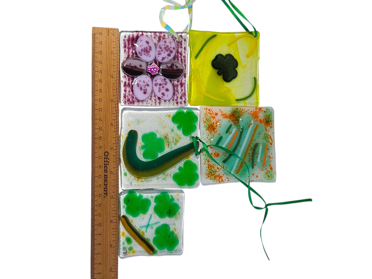 Five fused glass suncatcher ornaments beside a ruler, each about 3 inches square