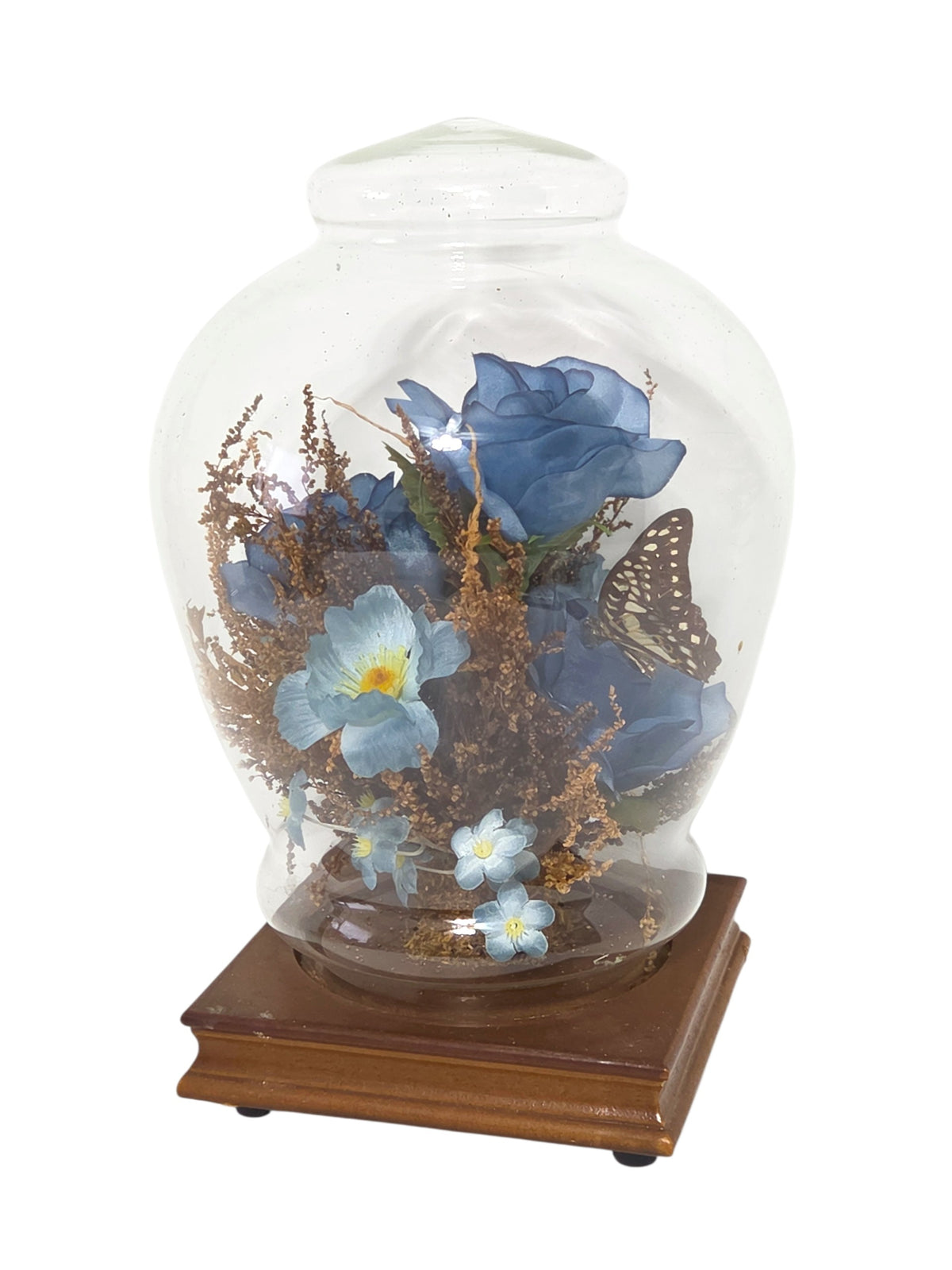 Glass dome cloche at an angle showing pale blue blooms, forget-me-nots and the butterfly among blue roses