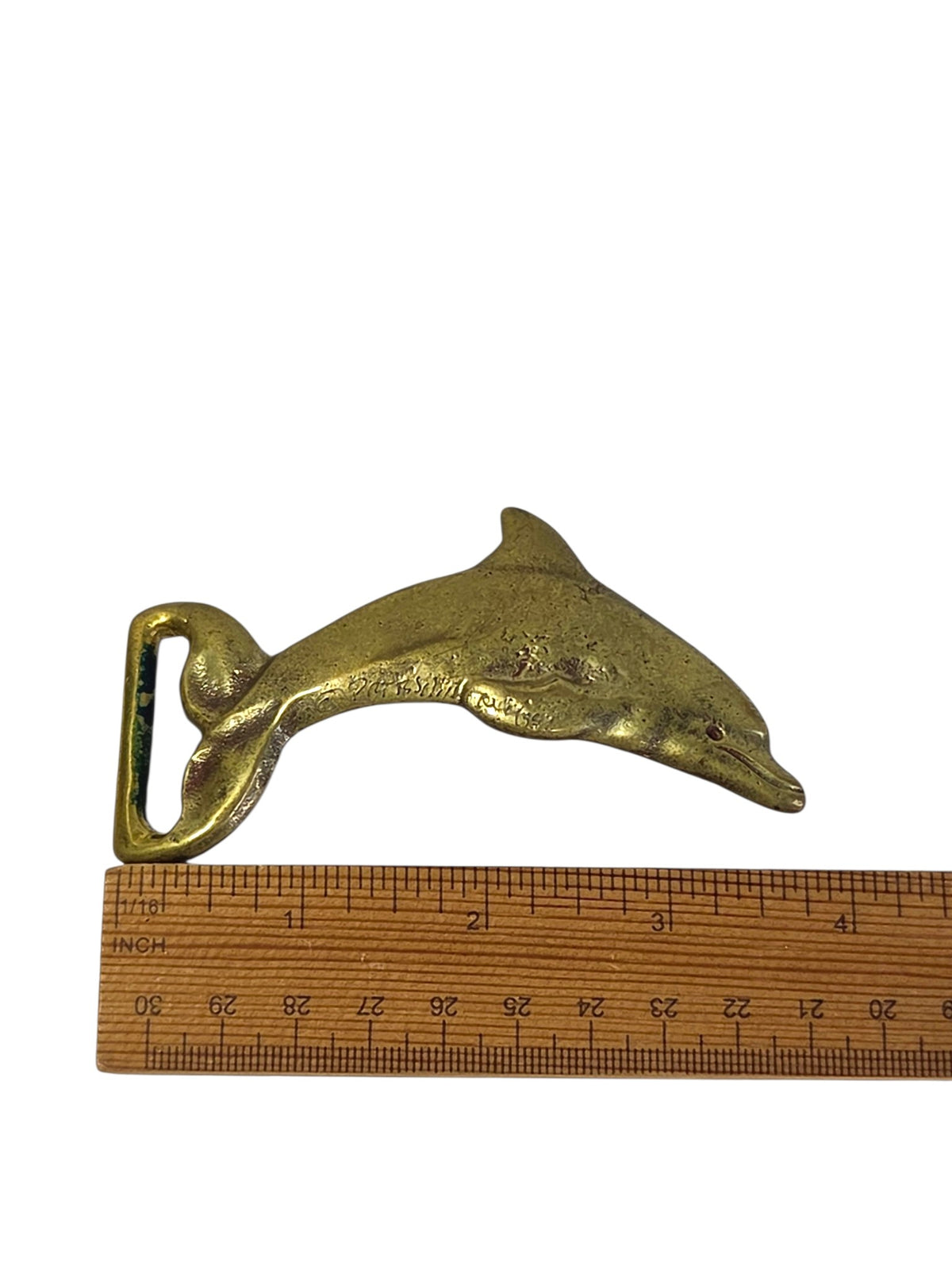 Brass dolphin belt buckle beside a ruler, about 3 7/8 inches long