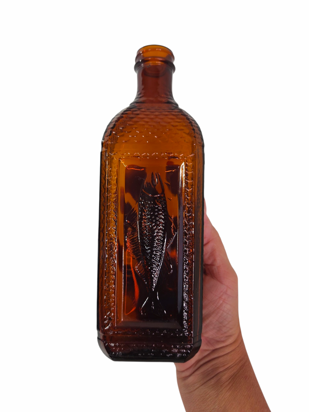 Oddly Darling Vintage amber glass bottle featuring an embossed fish design and textured scale sides held in a hand
