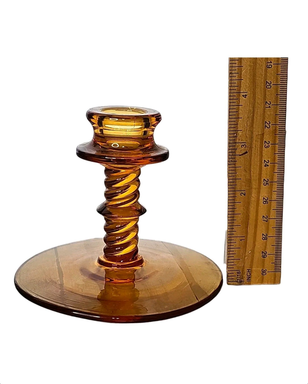 Oddly Darling Vintage amber glass candlestick holder with a twisted stem design and wide base next to a ruler.