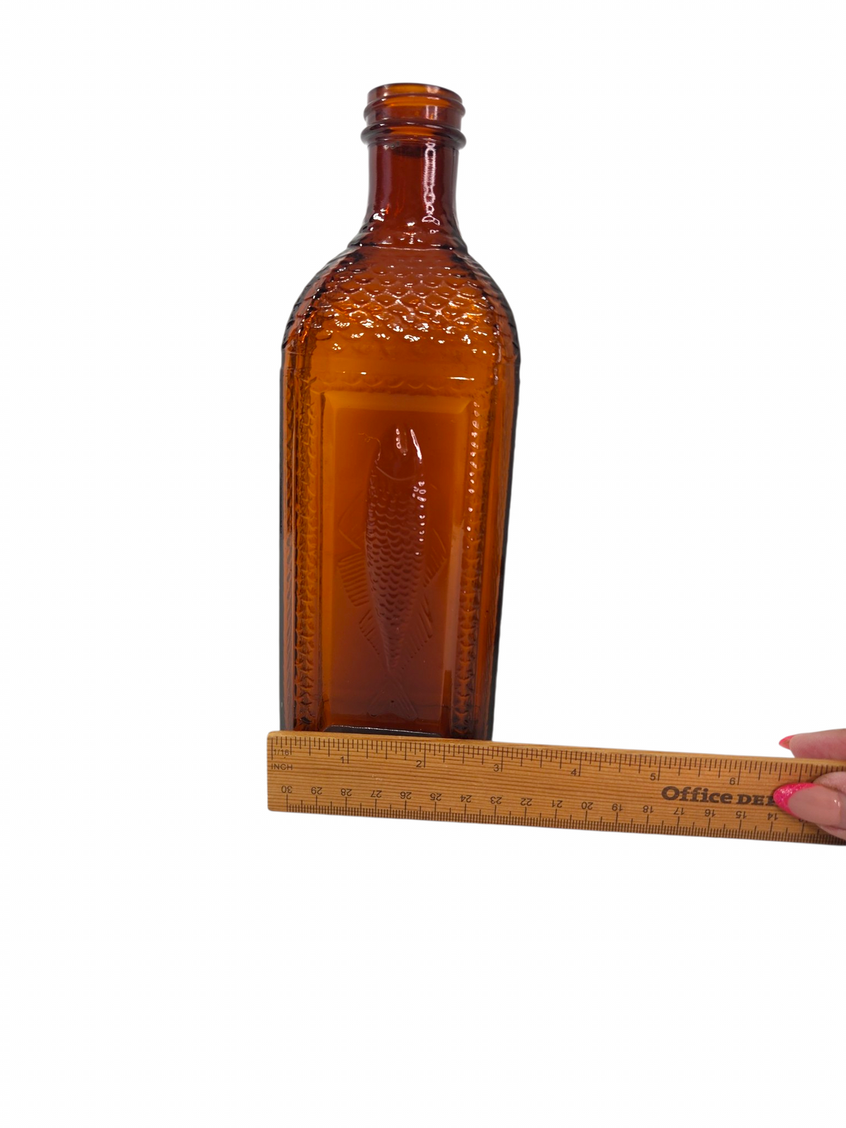 Oddly Darling Vintage amber glass bottle with an embossed fish design and textured scale sides held against a ruler.