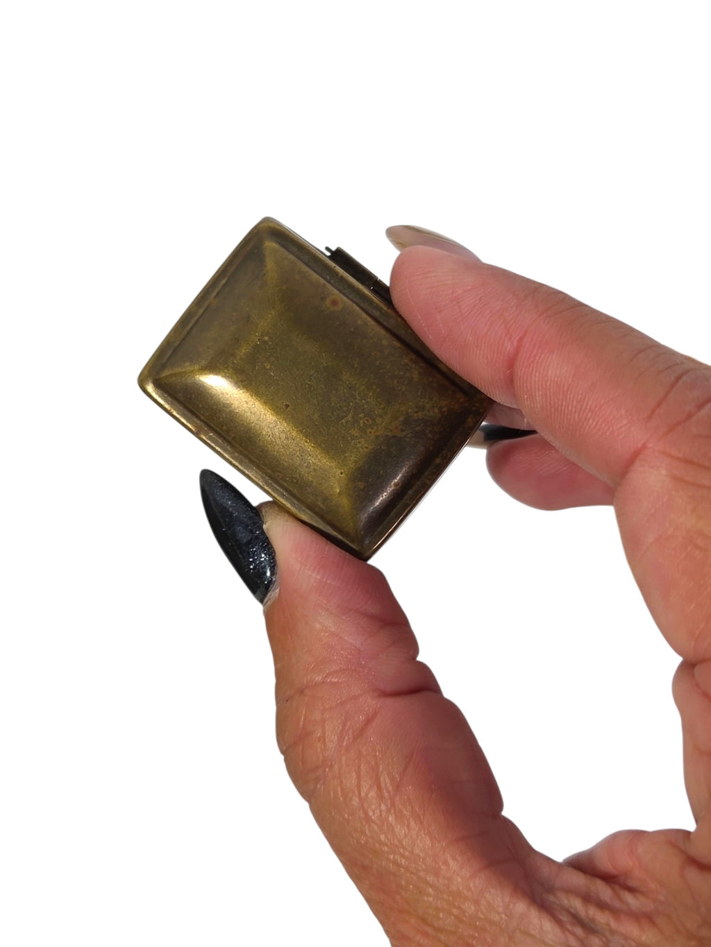 Small pillowed rectangular brass pill box with worn plating and spots, held between fingers