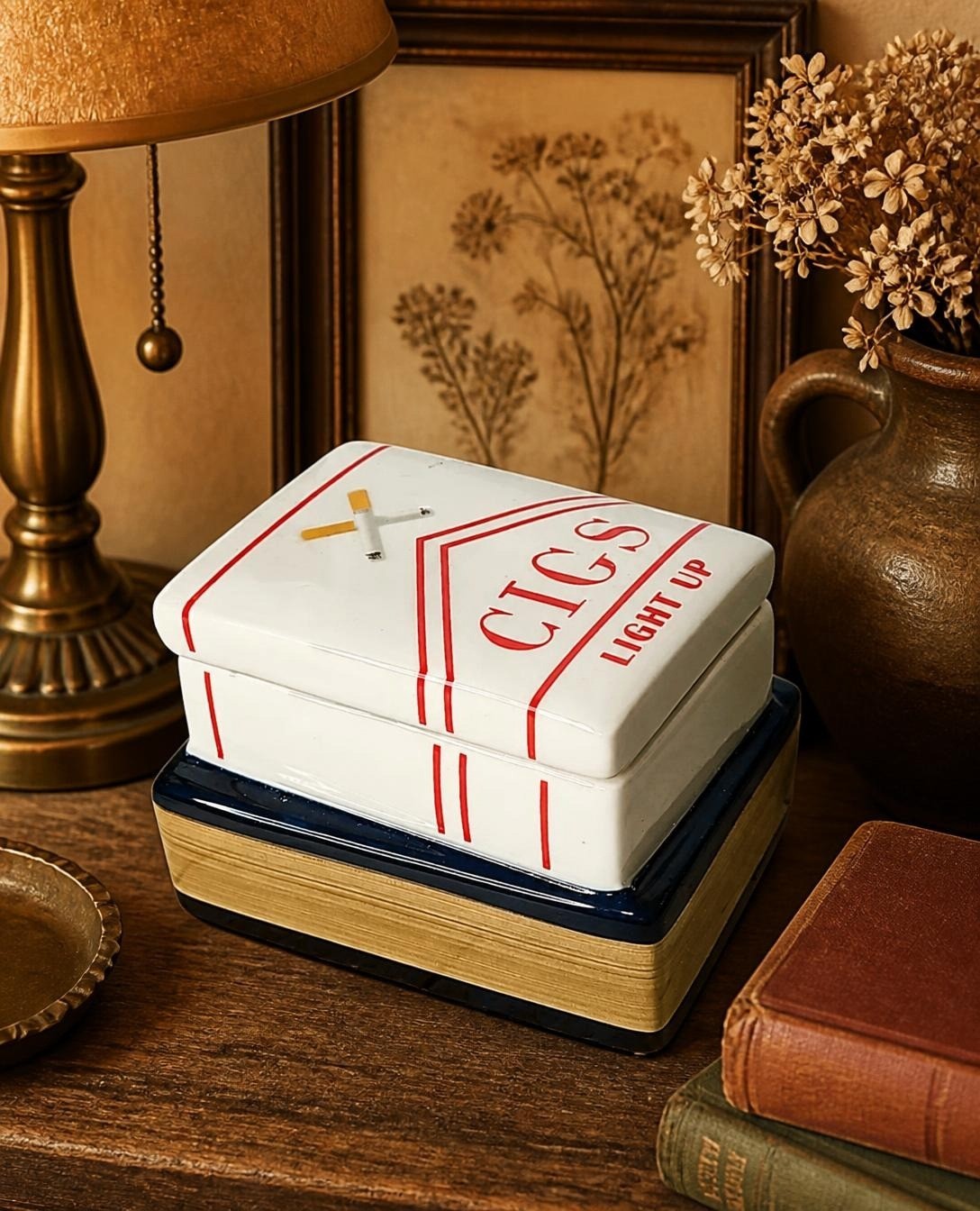 Oddly Darling Vintage ceramic trinket box shaped like a cigarette pack on a blue book base with gold page detailing.