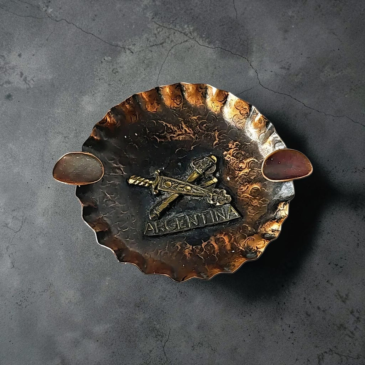 Oddly Darling Vintage hand-hammered copper ashtray with a brass Argentina emblem and crossed swords design.
