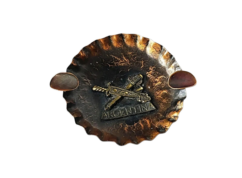 Oddly Darling Vintage hand-hammered copper ashtray with a brass Argentina emblem and crossed swords design.
