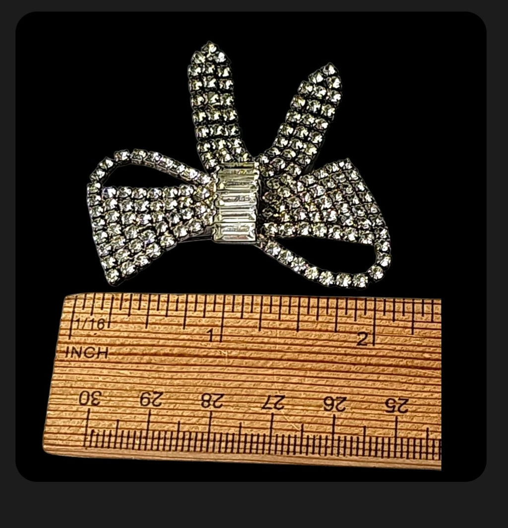 Oddly Darling Vintage crystal bow brooch with pave rhinestones and baguette center stone next to a wooden ruler