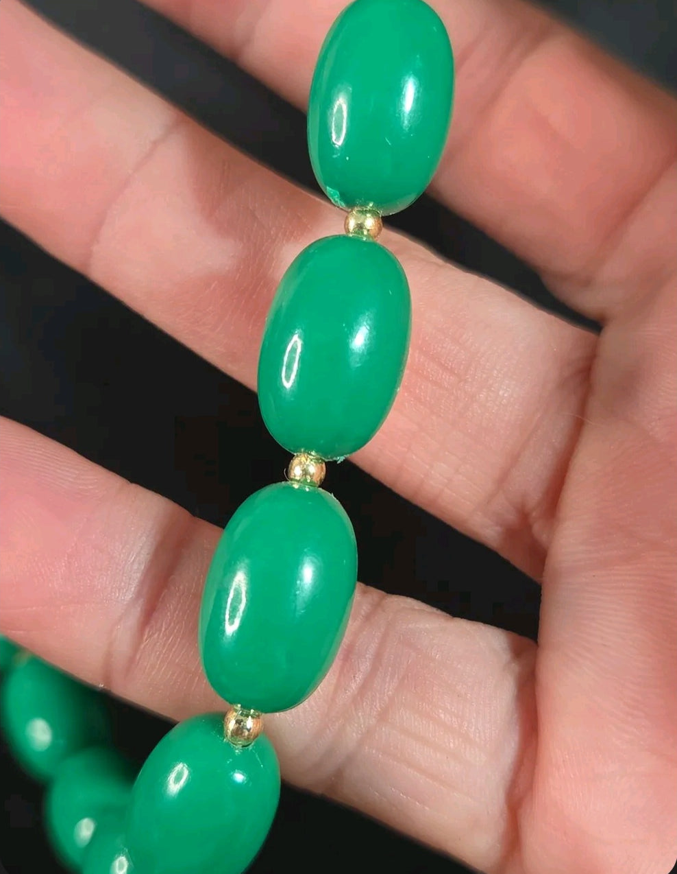 Oddly Darling Vintage emerald green oval bead necklace with gold-tone spacers held in a hand