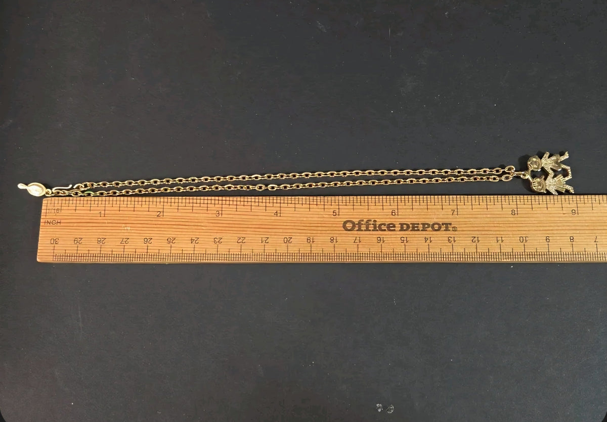 Oddly Darling Vintage gold-tone children charm pendant necklace measured against a wooden ruler on a black surface.