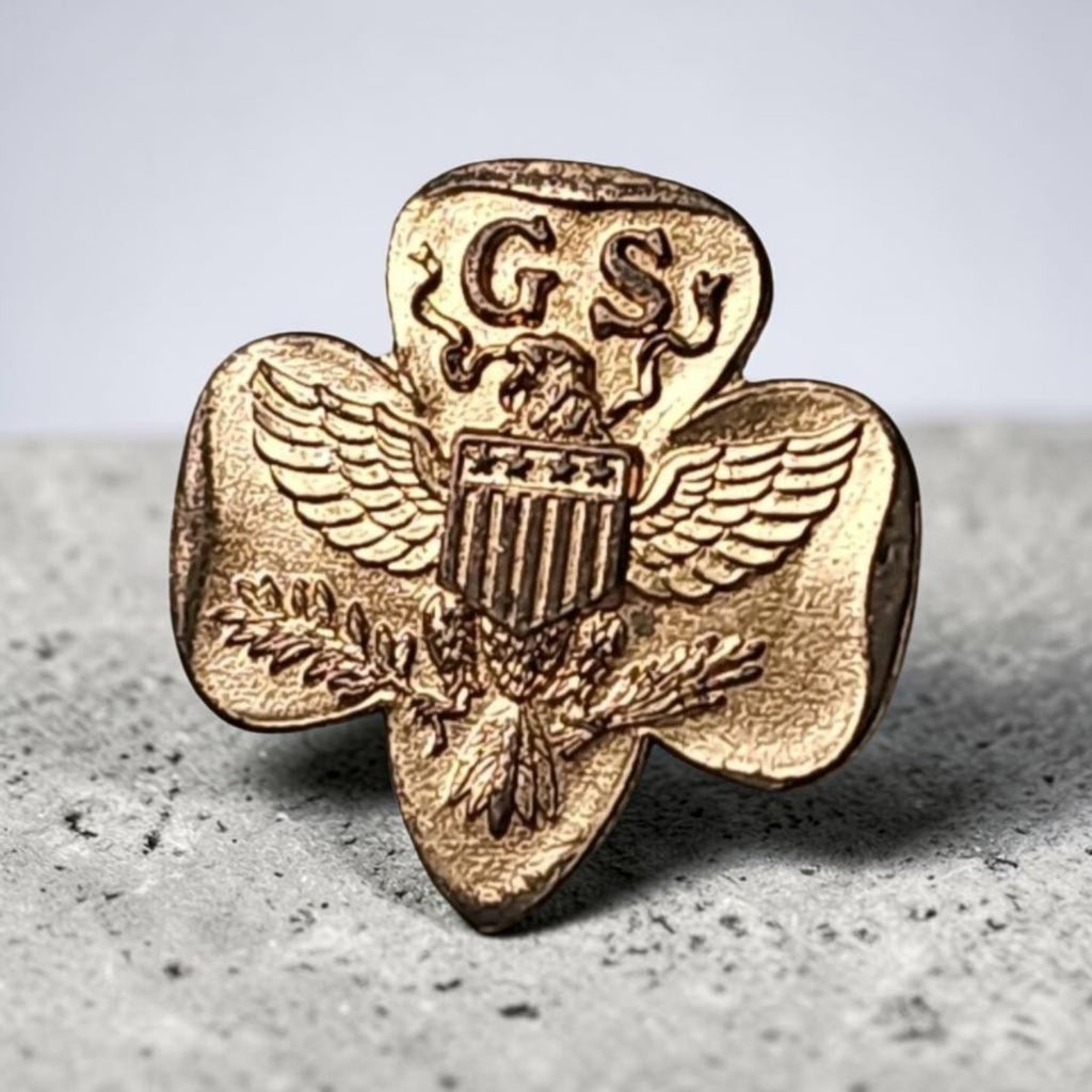Oddly Darling Vintage gold-tone Girl Scouts trefoil pin featuring an eagle and shield emblem on a textured surface.