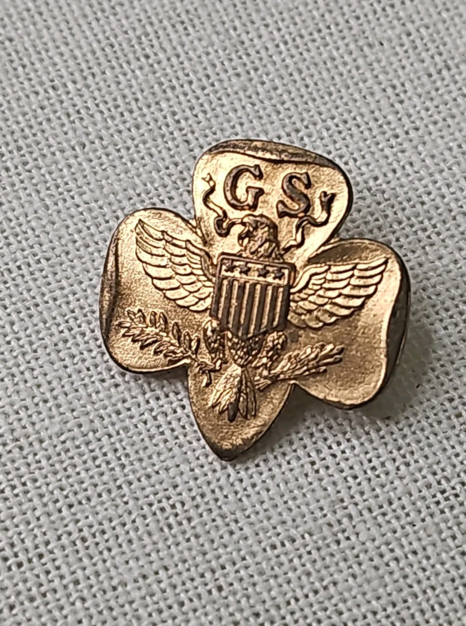 Oddly Darling Vintage gold-tone Girl Scouts trefoil pin featuring an eagle and shield emblem on a textured fabric background