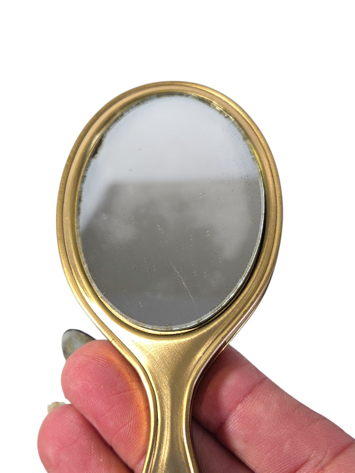 Front of the mini gold-tone hand mirror showing desilvering at the edge and a light scratch on the glass