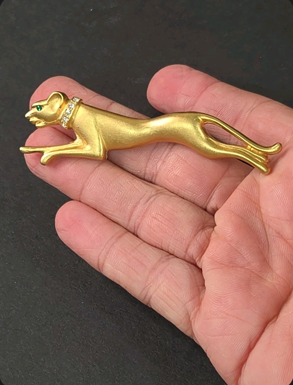 Oddly Darling Vintage brushed gold-tone panther brooch with crystal collar and green stone eye held in a hand.