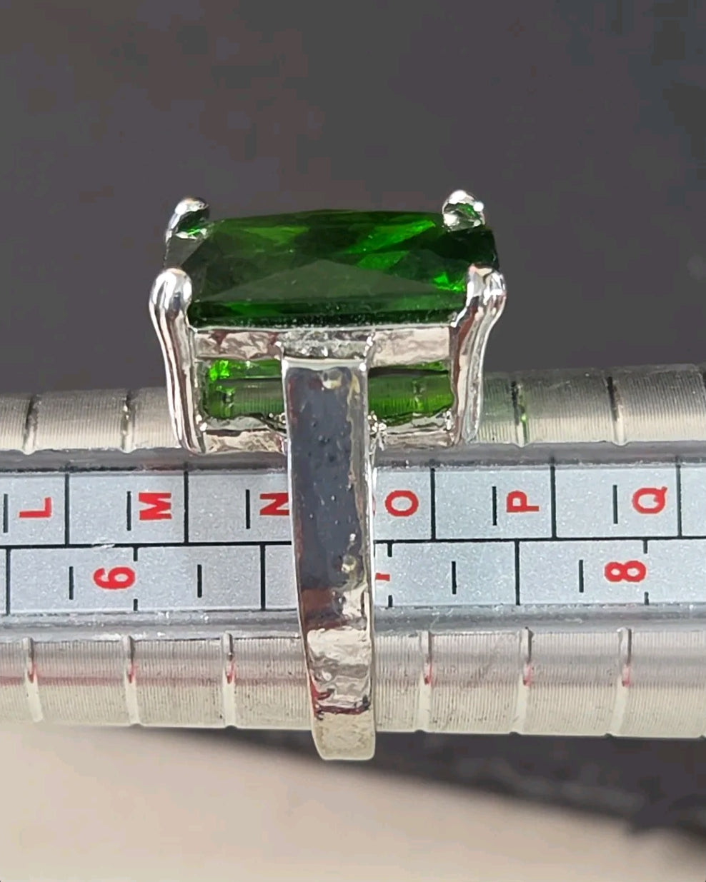 Oddly Darling Vintage emerald-cut green gemstone cocktail ring on a silver metal ring sizer tool