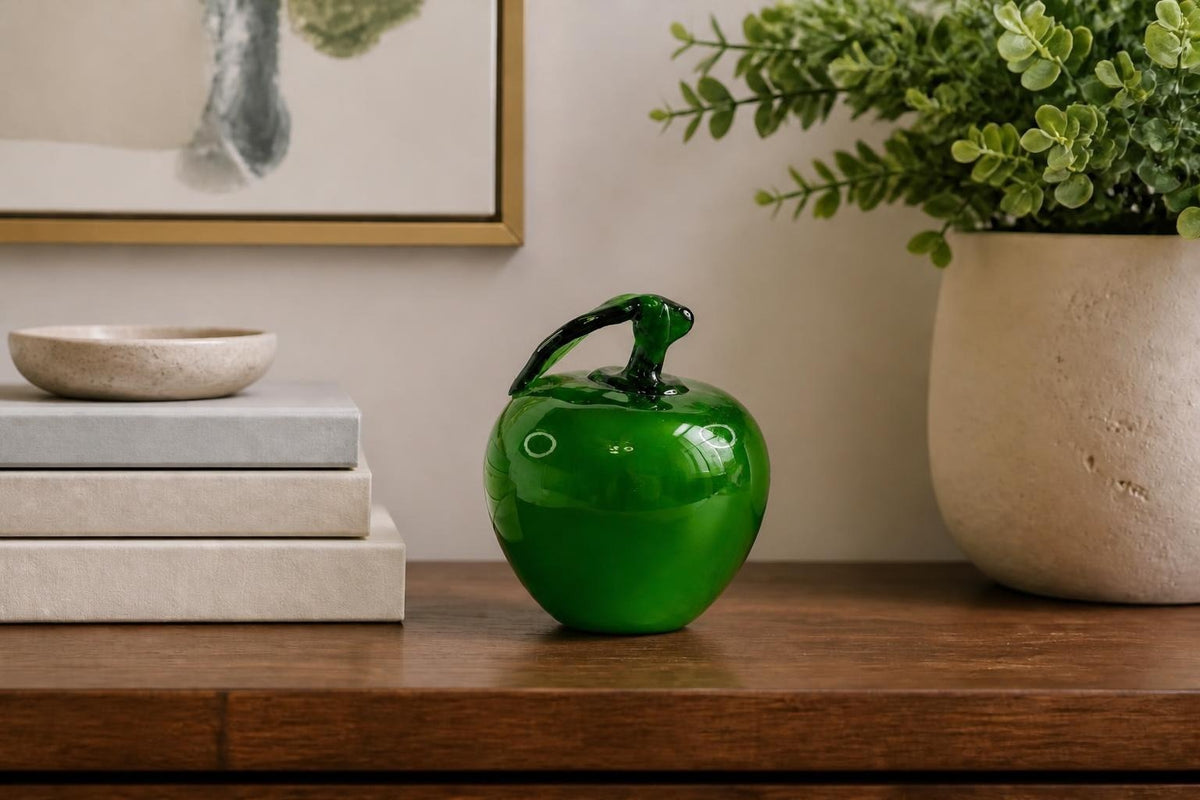 Oddly Darling Vintage hand blown green glass apple paperweight with a dark stem and leaf on a wooden desk