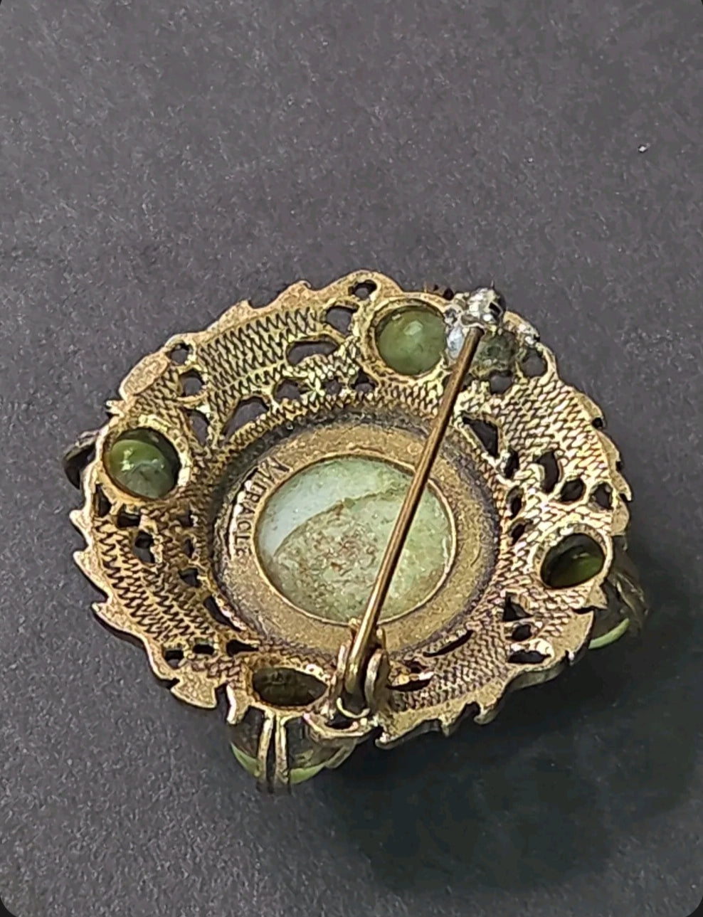 Back view of an Oddly Darling Vintage Miracle brooch showing the signature hallmark and antique-gold metal pin detail.