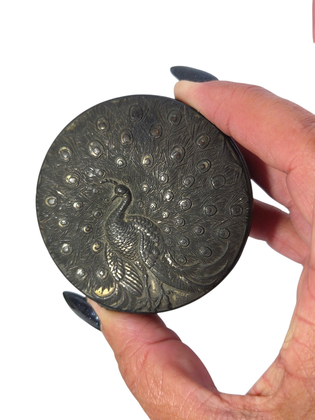 Lid of a round vintage box embossed with a full-tailed peacock in dark silver-tone patina, held in hand