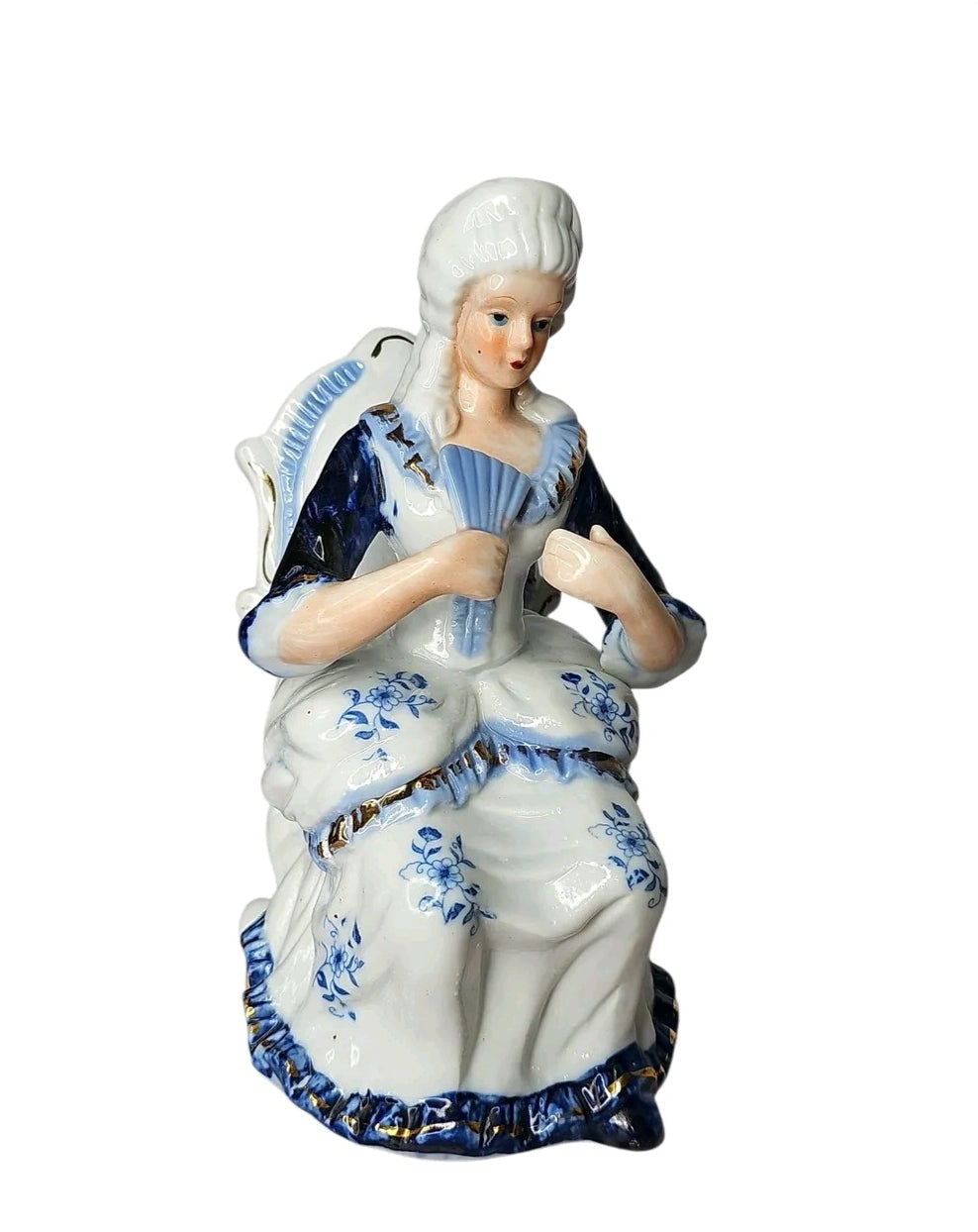 Oddly Darling Vintage porcelain lady figurine in a blue and white gown with gold trim, seated in a chair with a fan.