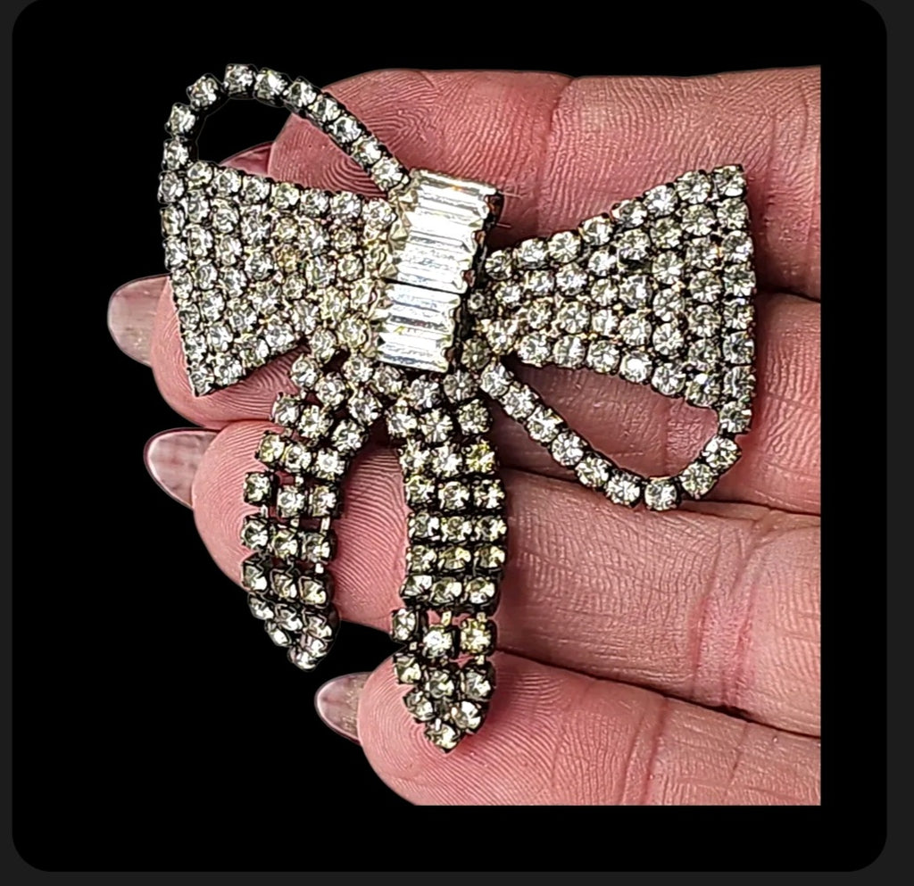 Oddly Darling Vintage crystal bow brooch featuring pave-set rhinestones and a baguette-cut center stone held in a hand.