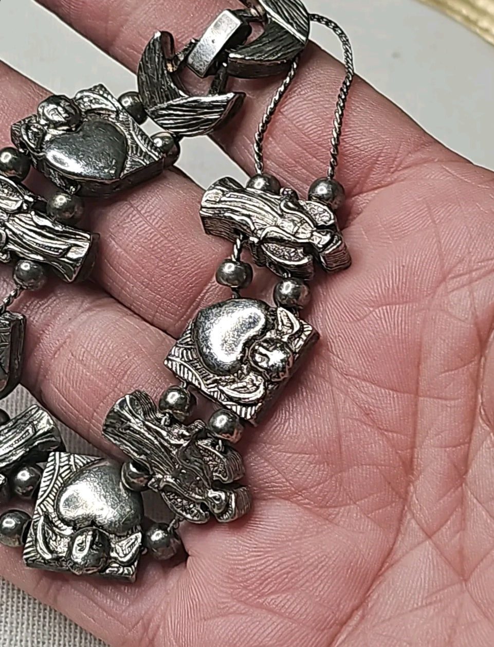 Oddly Darling Vintage silver-tone charm bracelet featuring detailed angel and heart motifs held in a hand.