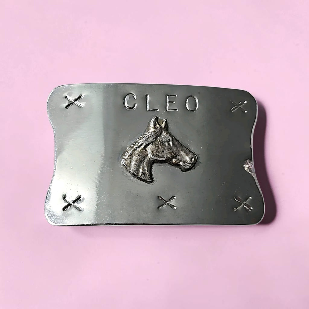 Oddly Darling Vintage silver-tone belt buckle with a horse head relief and the name CLEO on a pink background.