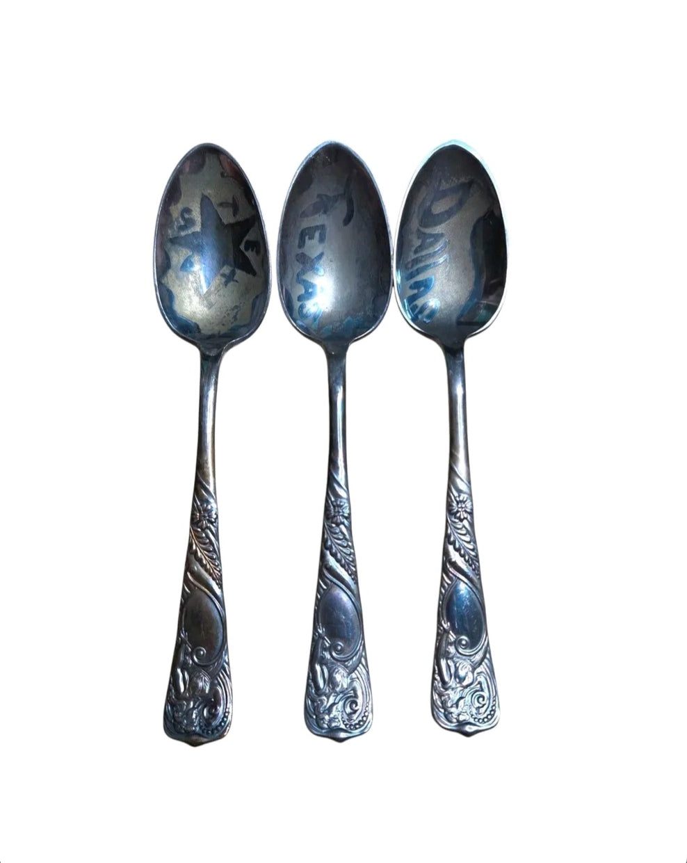 Oddly Darling Vintage set of three decorative metal spoons with ornate floral handles and Texas-themed engravings.